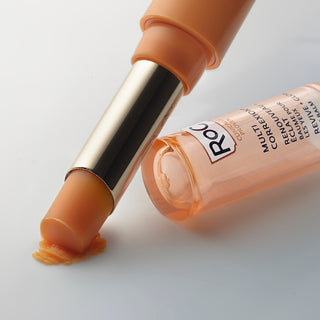 RoC Multi Correxion Revive + Glow Eye Balm in orange stick format with product smudged on surface to show texture.