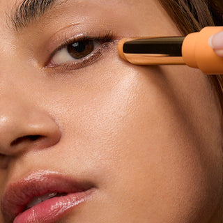 "Woman applying RoC Revive + Glow Eye Balm under her eye using the orange stick applicator.